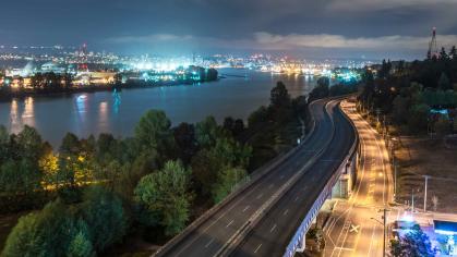 Cityscape at night from afar, including highway, river and glow of skyscrapers in distance