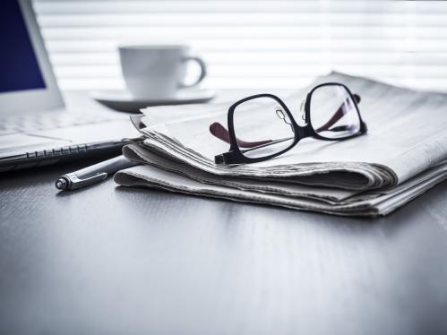 Newspaper laying on table with glasses and laptop